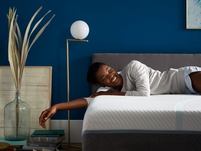 Woman laughing on a bed placed on a gray frame with a gold lamp and books on the floor