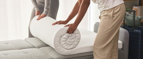 Two women unrolling a Tempur-Cloud topper on a sofa bed
