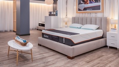 A retail display unit showcasing the Tempur-Luxe Adapt Queen Firm 13 inch foam mattress with two pillows resting on top