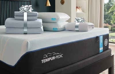 A Tempur-Pedic sheet set and pillows on a mattress with a silver gift bow around them.