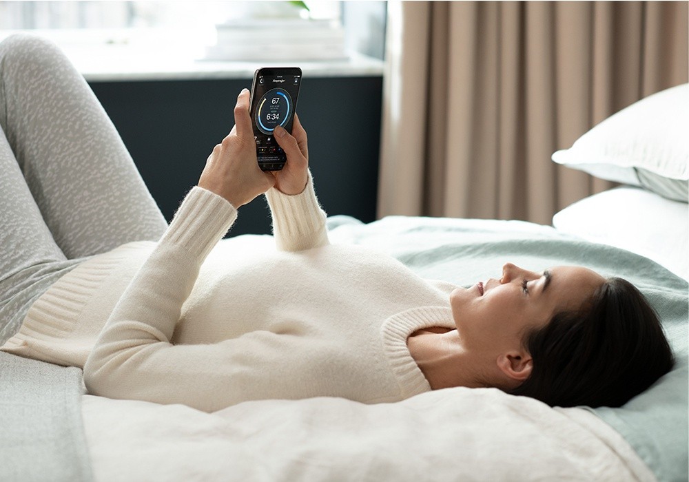 A woman lying on a Tempur-Pedic mattress with an Ergo Smart Base checking her sleep score on her phone