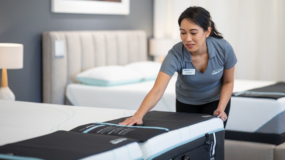 A store associate straightening the bedding on a mattress