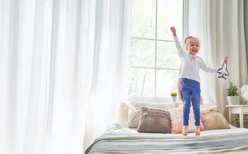 A little girl jumping on a bed with a Rocket Ship in hand