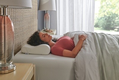 Lady wearing pink shirt sleeping on a mattress with neck pillow