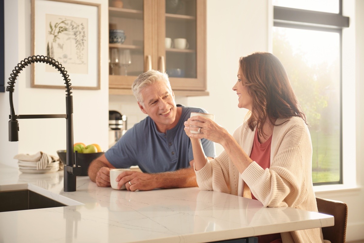 Man and woman sitting in the kitchen having a cup of coffee in front of large window