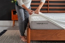 Man putting removable tempur mattress protector on corner of mattress