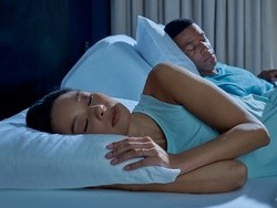 A couple laying on a split king mattress, woman raised for snoring