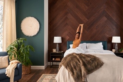 A woman sitting in bed stretching, looking out the window next to a wood accent wall in a decorated room