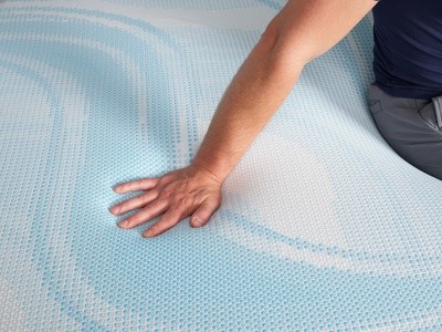 Man sitting on a LuxeBreeze mattress with his hand pressed into the mattress