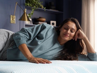 A woman laying on her side in a green sweatshirt on a mattress