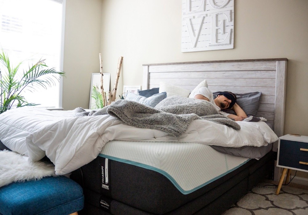 A man wearing a Tempur Sleep Mask laying on a Tempur-Pedic mattress