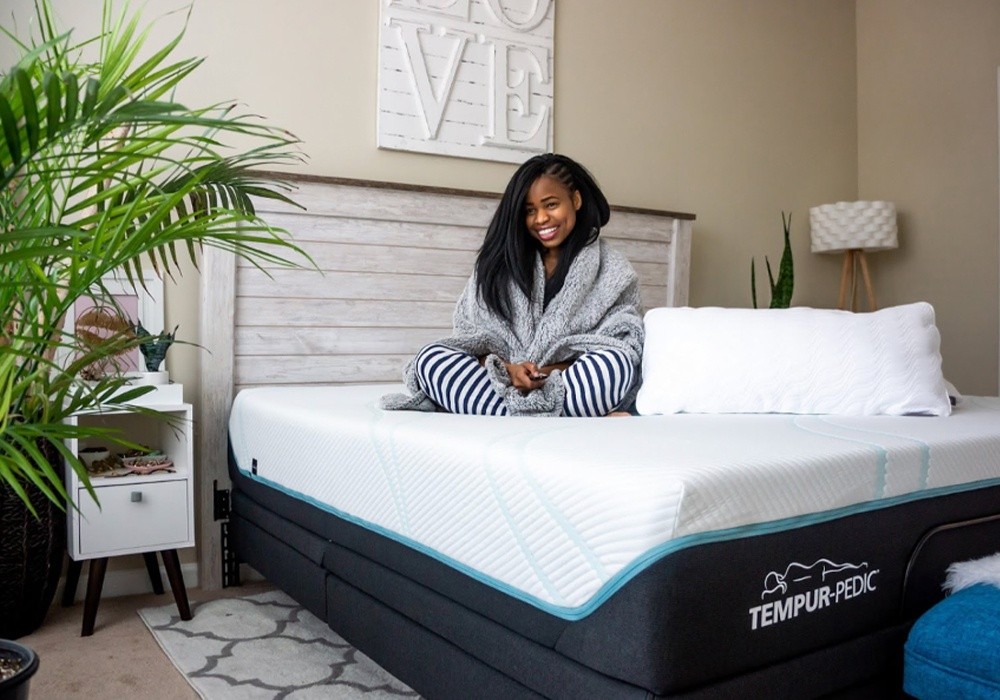 A smiling woman sitting on a Tempur-Pedic Mattress