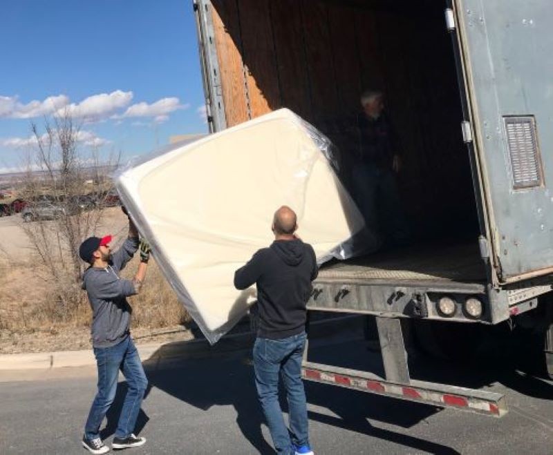 Two men unloading mattress from truck