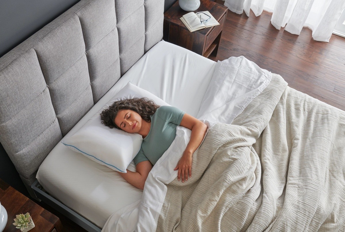 woman in green shirt asleep in bed in a dressed room with gray headboard and white bedding