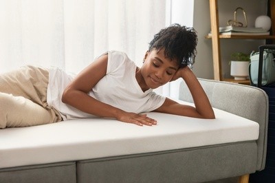 woman laying on futon couch with the Adapt topper laying over it