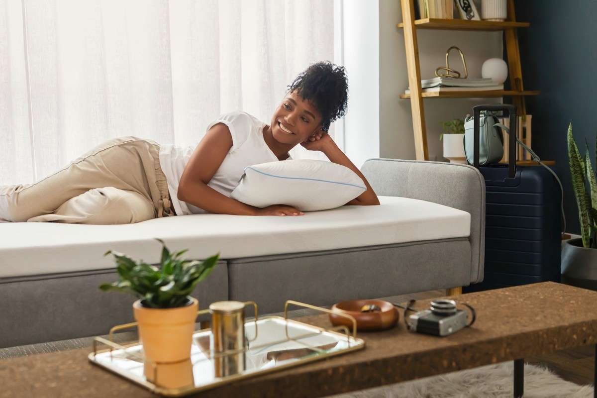 woman laying on grey futon with Adapt topper on top and a pillow under her side