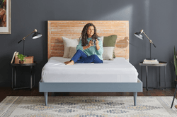 woman holding cup sitting on mattress with protector