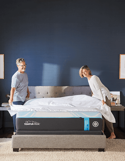 Couple in a fully dressed bedroom, putting sheets on their Queen, Soft, LuxeBreeze mattress - mobile view