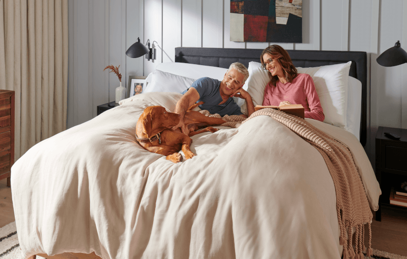 Man and woman lying on Tempur-Pedic mattress with brown dog