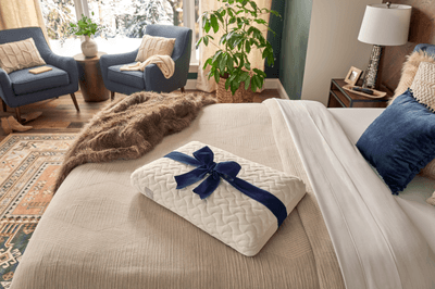 Tempur cloud pillow sitting on dressed bed with two blue chairs in the background.png