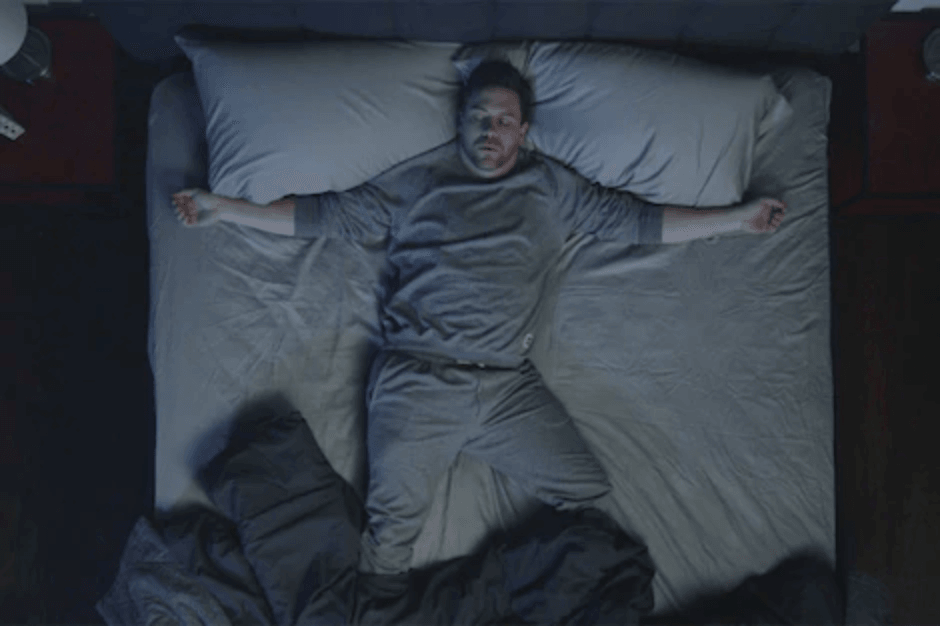 a man in bed, covers thrown off from sleeping hot