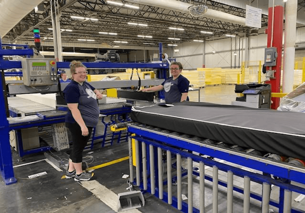 two woman standing in a factory smiling.png